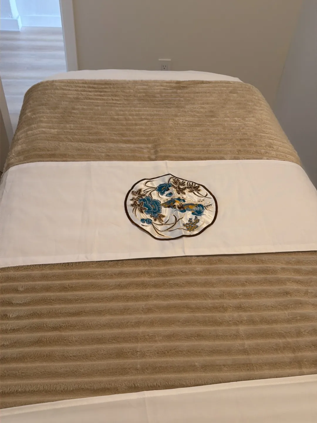 Embroidered table runner laid across a made massage table in a treatment room at Harbor Wellness Massage in San Carlos